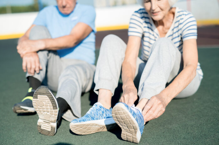 Senior Couple Tying Shoes on Track Mid section portrait of white haired senior couple tying sports shoes sitting on running track outdoors, copy space